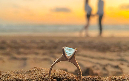 A couple on a beach at sunset showing aquamarine rings, with aquamarine gems displayed on the side.