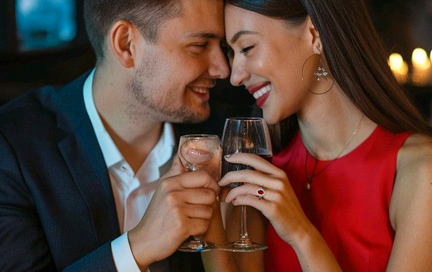 An elegant couple enjoying a romantic dinner, with the woman wearing a ruby ring or pendant.