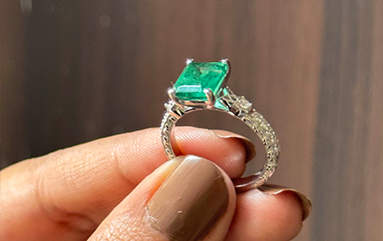 A woman holding her emerald ring beside an open jewelry box on her vanity.