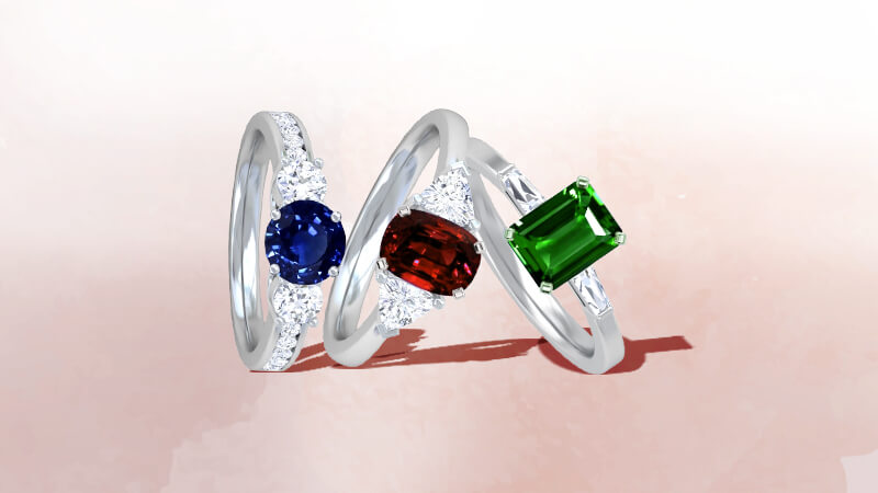 Emerald, ruby, and sapphire three stone rings with diamonds